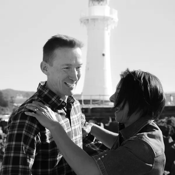 A couple in front of a lighthouse, looking at each other.