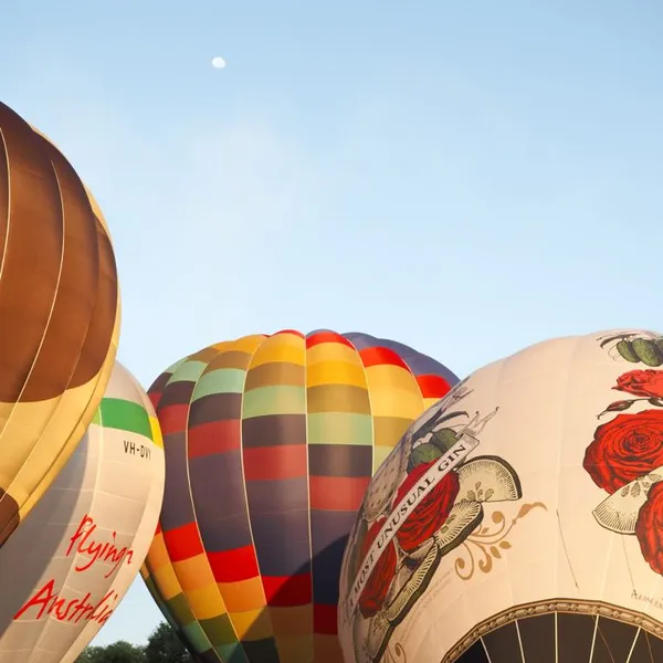 4 hot air balloons in the sky, with the moon rising in the background.