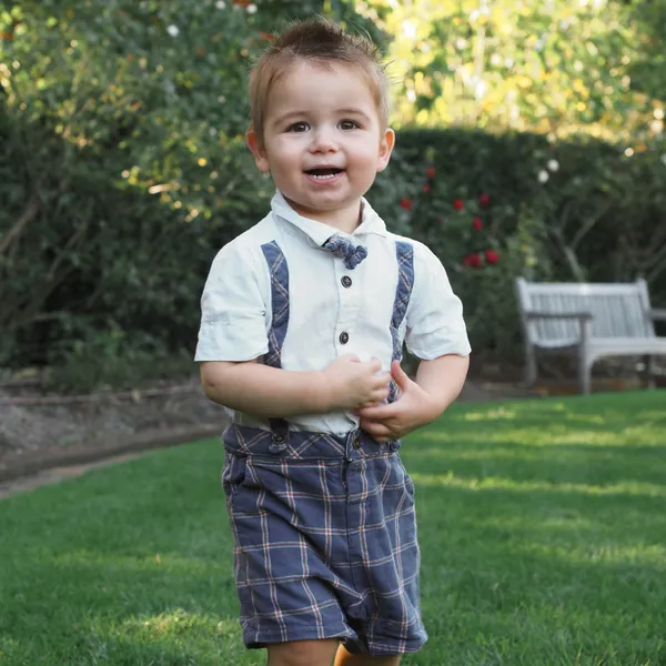 A toddler boy smiling in a green grassy scene.